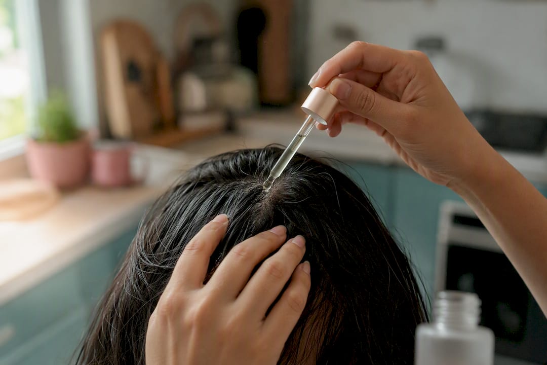 Hands applying tonic drops onto scalp